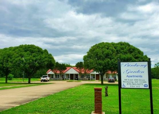 Birdsong Garden Apartments in Birdsong, Arkansas — red-roofed building with manicured lawn and property sign under a cloudy sky