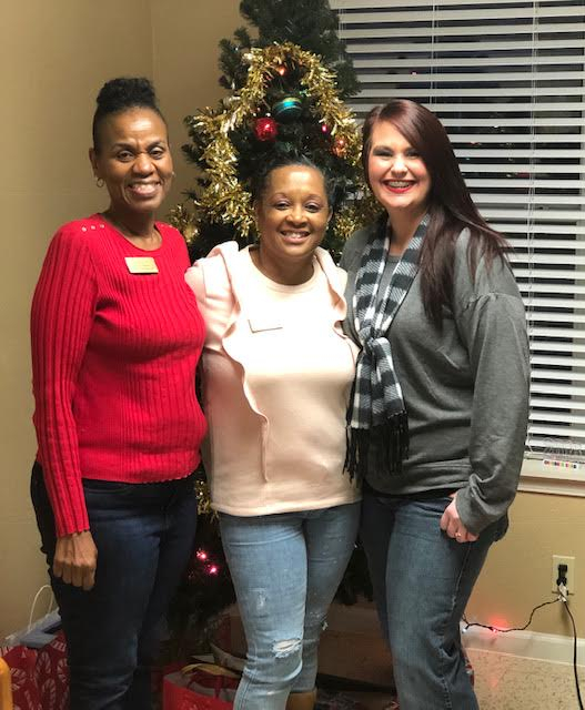Women smiling at a Christmas tree office holiday celebration