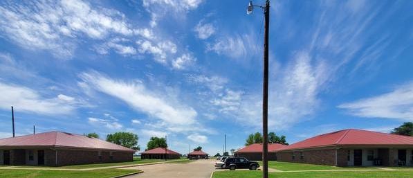 Luxora Garden Apartments in Luxora, Arkansas — brick buildings with red roofs flanking a wide driveway under a dramatic blue sky