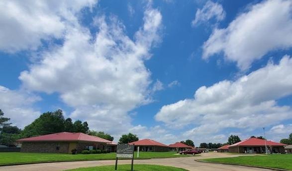 Osceola Garden Apartments in Osceola, Arkansas — brick buildings with red roofs and manicured lawn under a bright blue sky